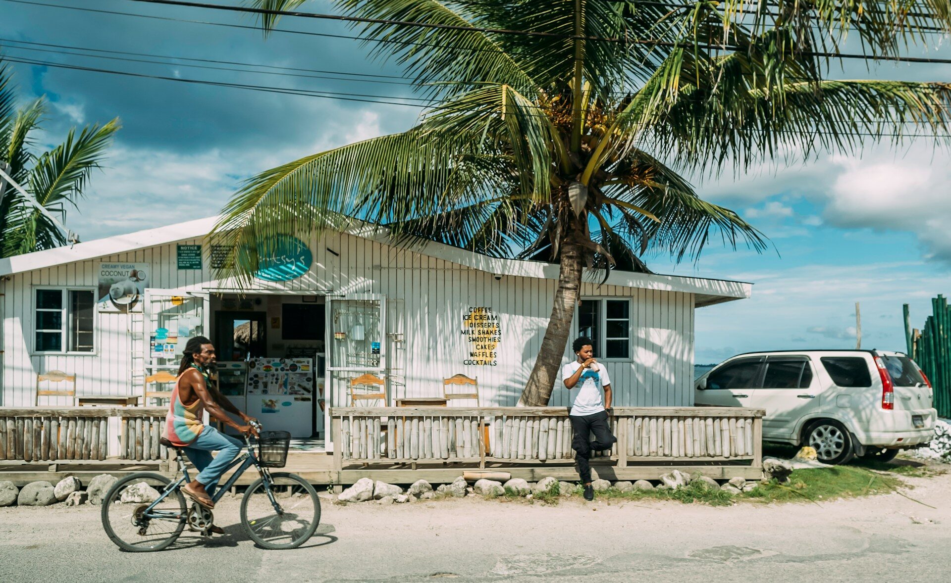 Street scene in Jamaica with local shop, palm trees and two people outdoors